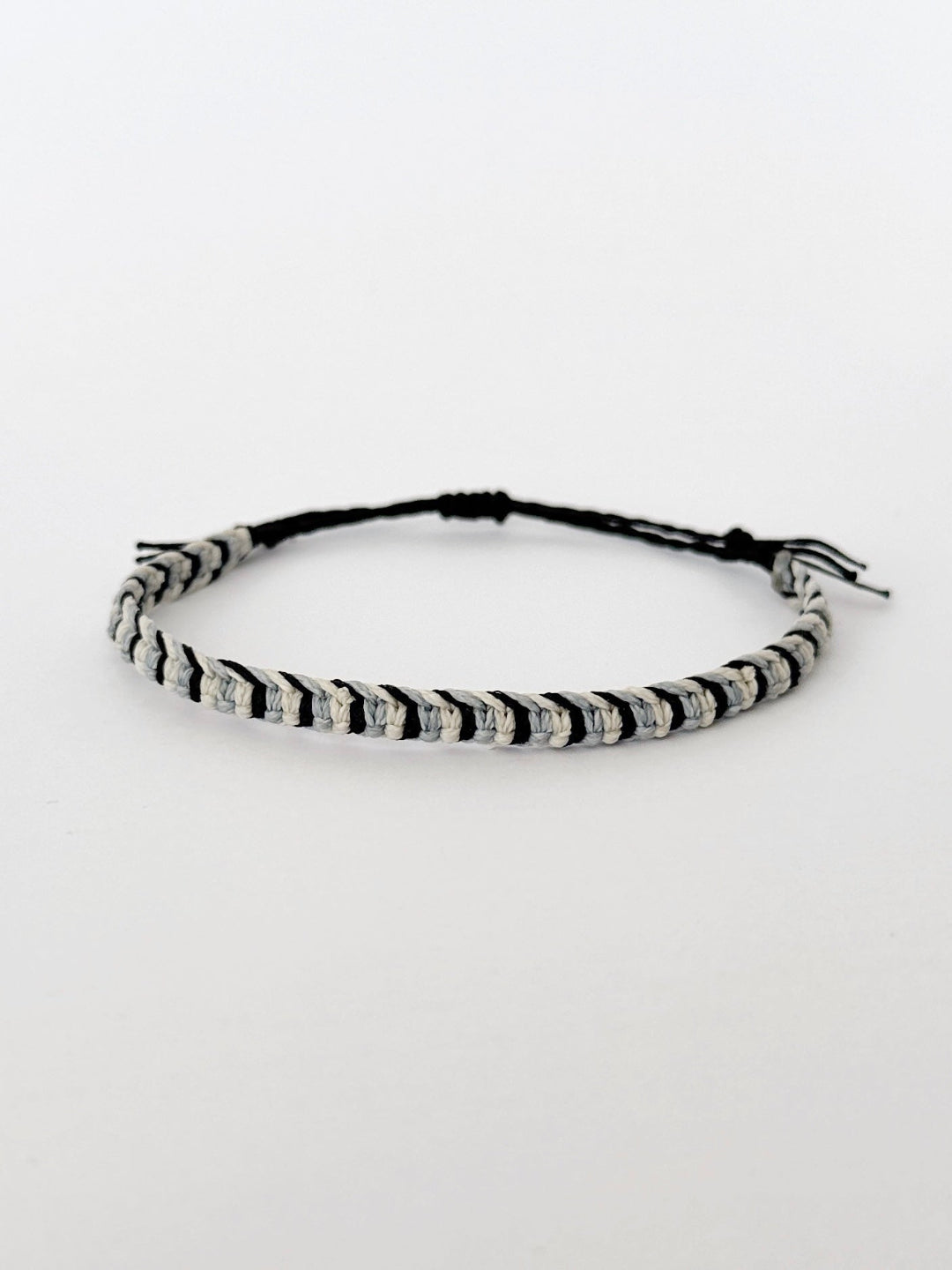 צמיד Tide מקרמה לגבר בעבודת יד על רקע בהיר, בגווני שחור ותכלת-אפרפר.