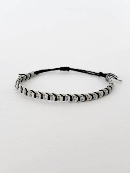 צמיד Tide מקרמה לגבר בעבודת יד על רקע בהיר, בגווני שחור ותכלת-אפרפר.