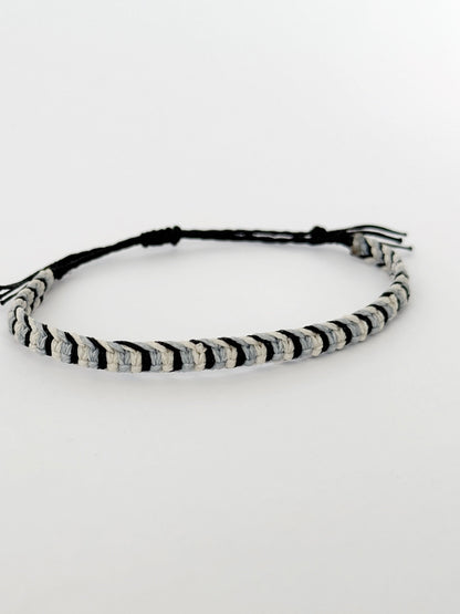 צמיד Tide מקרמה לגבר בעבודת יד על רקע בהיר, בגווני שחור ותכלת-אפרפר.