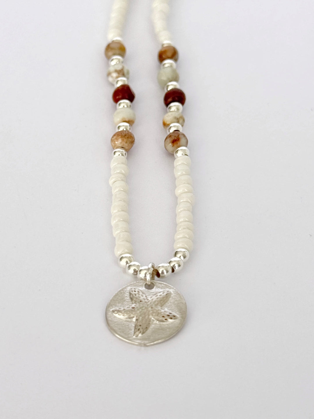 שרשרת Mirage היא שרשרת חרוזים עדינה בעבודת יד, בגוונים חמים של לבן, קרם ואדמדם. השילוב בין החרוזים הקטנים לבין אלמנט הכסף יוצר מראה רגוע ונקי, כזה שמרגיש כמו קו של אור על חול חם.