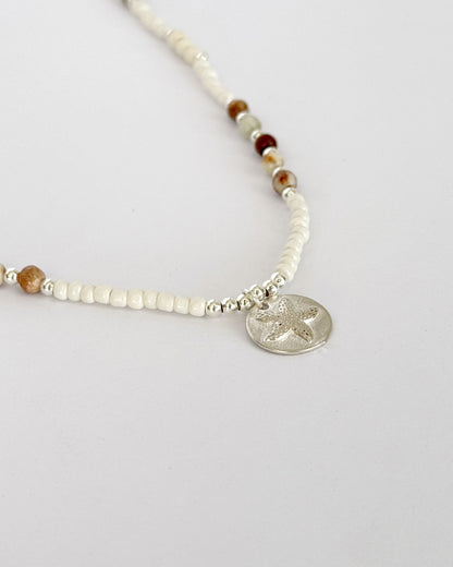 שרשרת Mirage היא שרשרת חרוזים עדינה בעבודת יד, בגוונים חמים של לבן, קרם ואדמדם. השילוב בין החרוזים הקטנים לבין אלמנט הכסף יוצר מראה רגוע ונקי, כזה שמרגיש כמו קו של אור על חול חם.