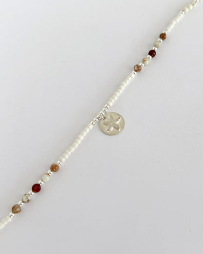 שרשרת Mirage היא שרשרת חרוזים עדינה בעבודת יד, בגוונים חמים של לבן, קרם ואדמדם. השילוב בין החרוזים הקטנים לבין אלמנט הכסף יוצר מראה רגוע ונקי, כזה שמרגיש כמו קו של אור על חול חם.