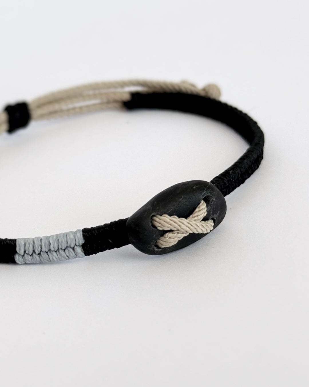 תקריב של חלוק נחל כהה משולב בצמיד מקרמה בעבודת יד, קשר גלוי ועיצוב מינימליסטי